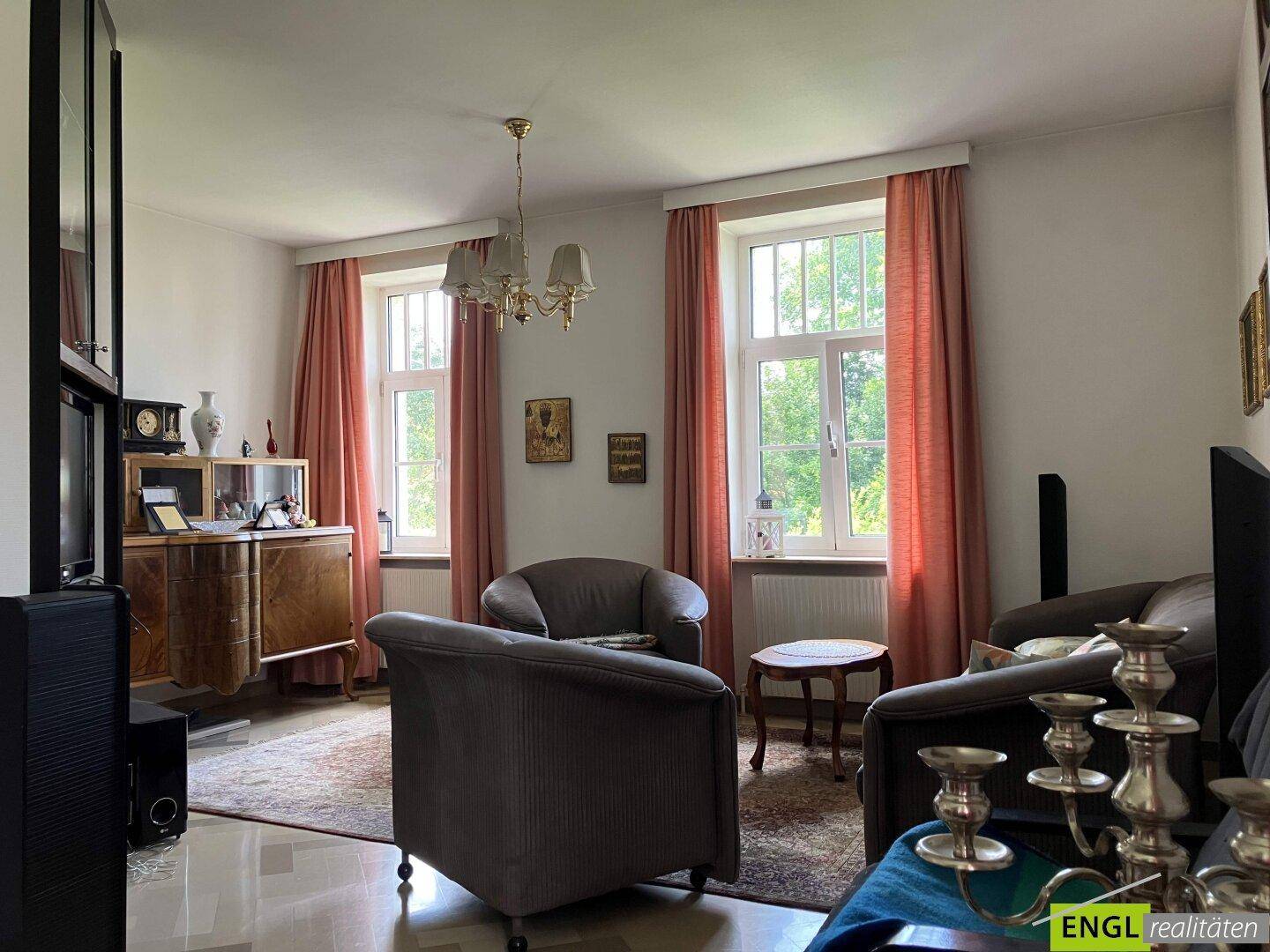 Gemütliches Wohnzimmer mit zwei Fenstern, die viel Tageslicht hereinlassen, und traditionellen Möbeln.