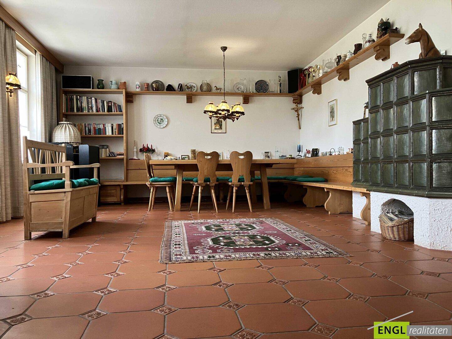 Rustikaler Essbereich mit großem Holztisch, Sitzbank und einem traditionellen Kachelofen.