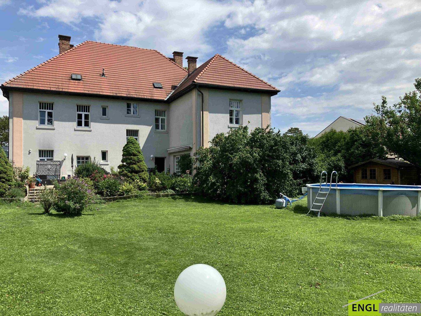 Das Haus von außen mit einem gepflegten Garten und einem Aufstellpool unter blauem Himmel.