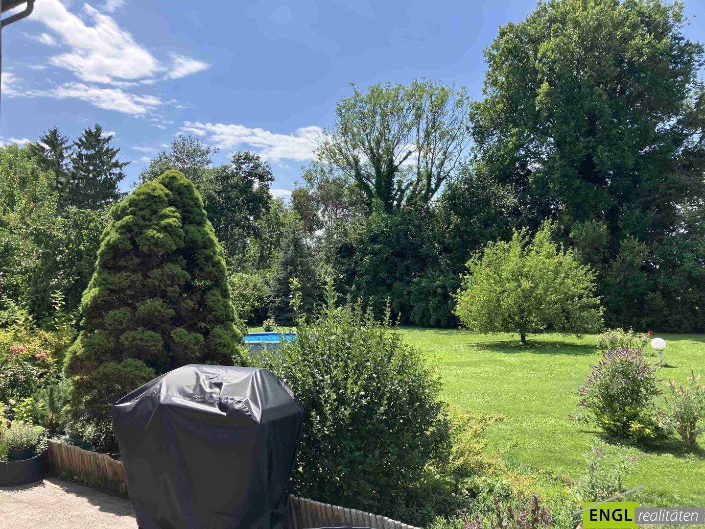 Üppiger, grüner Gartenbereich mit hohen Bäumen und einem Grillplatz im Freien.