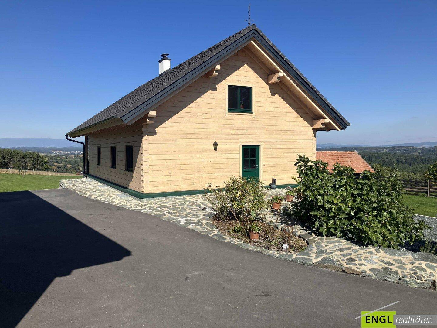 Charmantes Holzhaus mit grünen Fensterrahmen und gepflastertem Vorplatz.