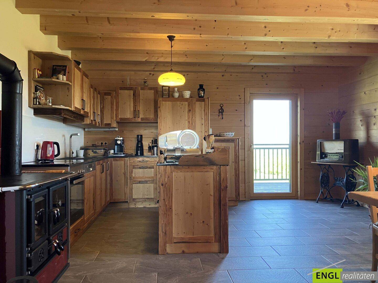 Rustikale Holzküche mit traditionellem Ofen, Holzbalken und Zugang zum Balkon.
