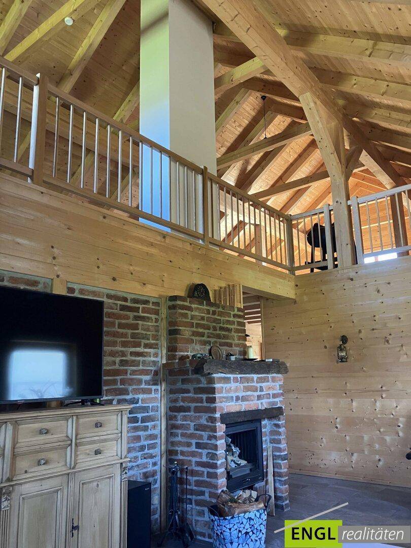 Hoher Wohnbereich mit Ziegelkamin, Holzwänden und offener Galerie.