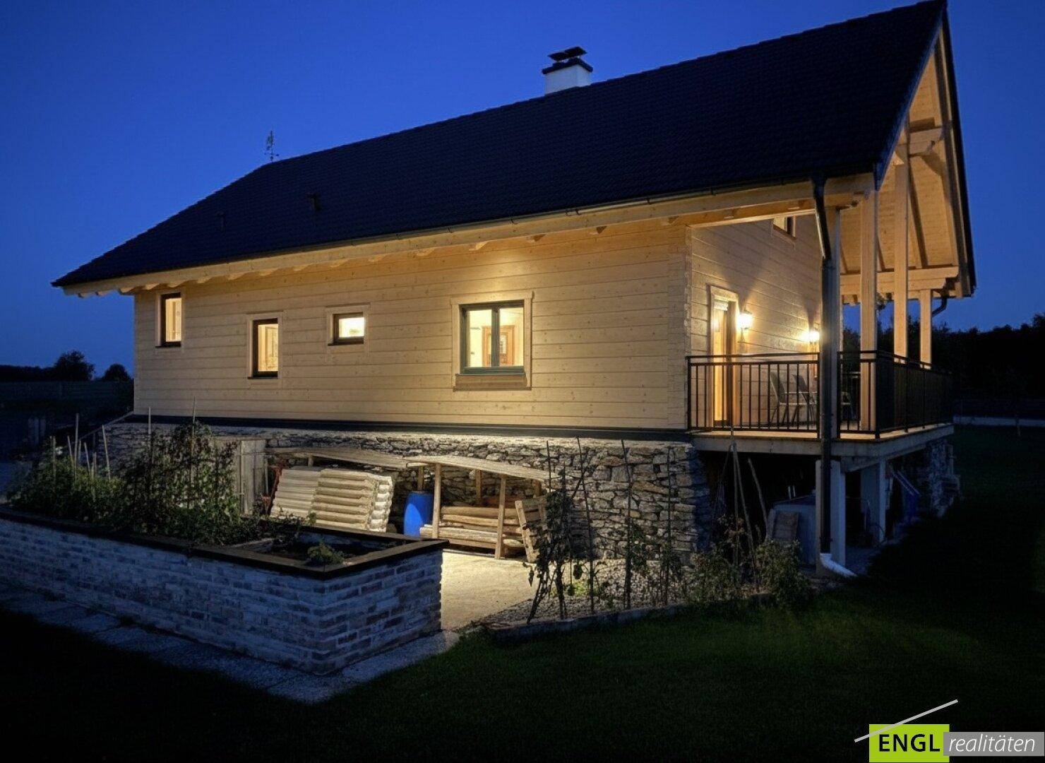 Holzhaus bei Nacht mit beleuchteter Fassade und Balkon unter dunklem Himmel.