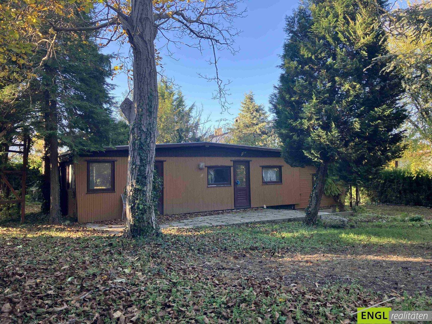 Ansicht eines einfachen Bungalows mit Holzverkleidung und umgebendem Gartenbereich.