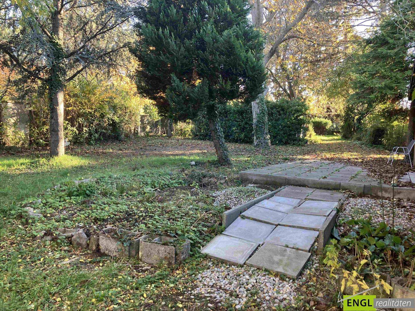 Gartenbereich mit einer kleinen gepflasterten Terrasse und umgebender Vegetation.