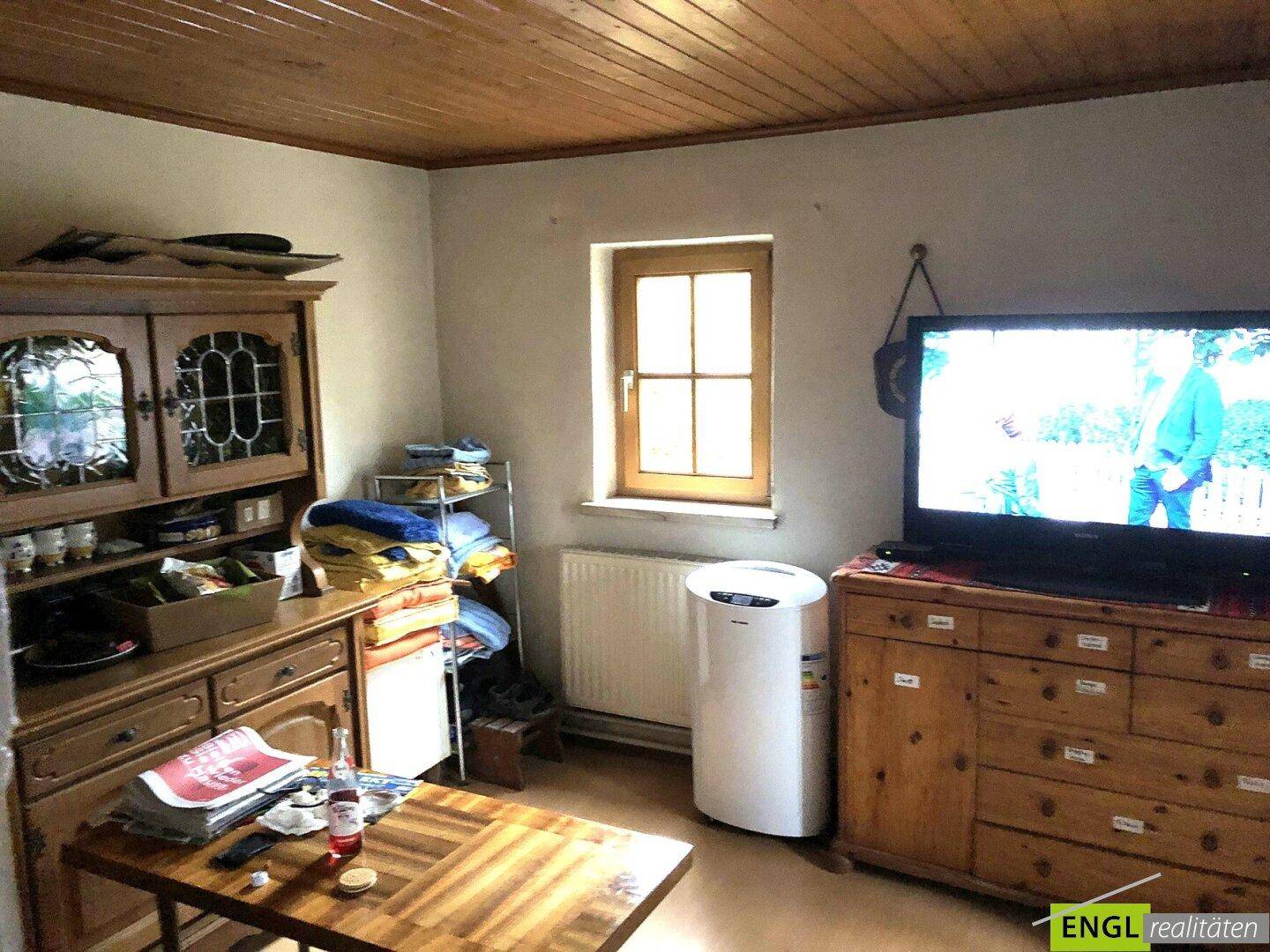 Gemütliches Wohnzimmer mit Holzdecke, rustikalen Möbeln und einem Fenster, das natürliches Licht hereinlässt.