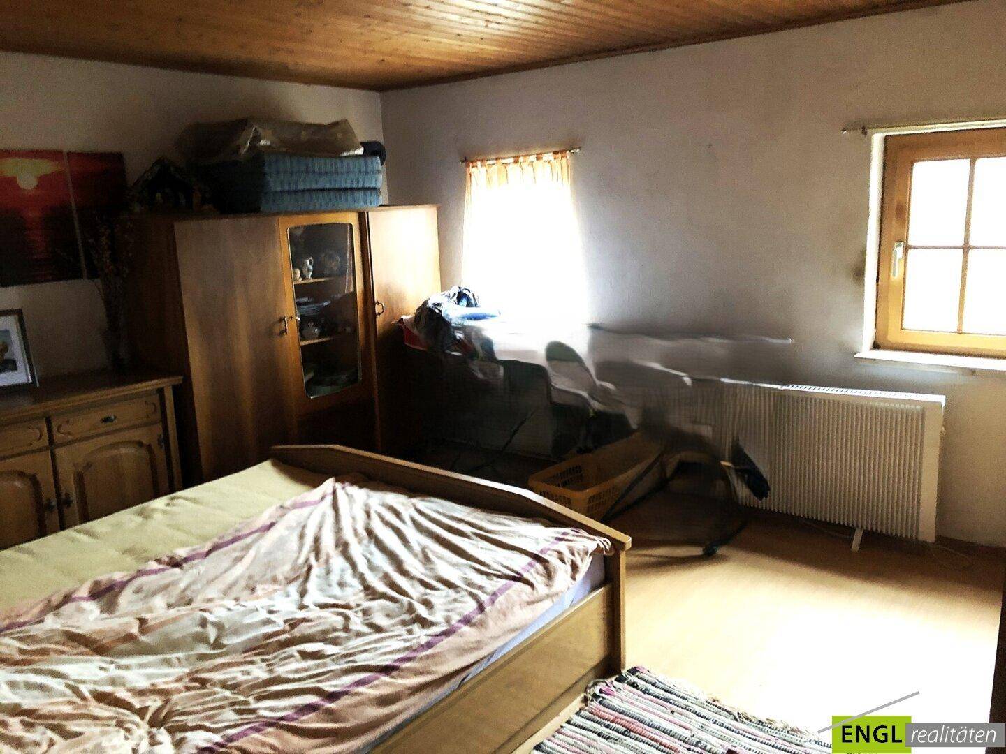 Schlafzimmer mit Holzdecke und einem Fenster, das für natürliche Belichtung sorgt, ausgestattet mit einem Bett.