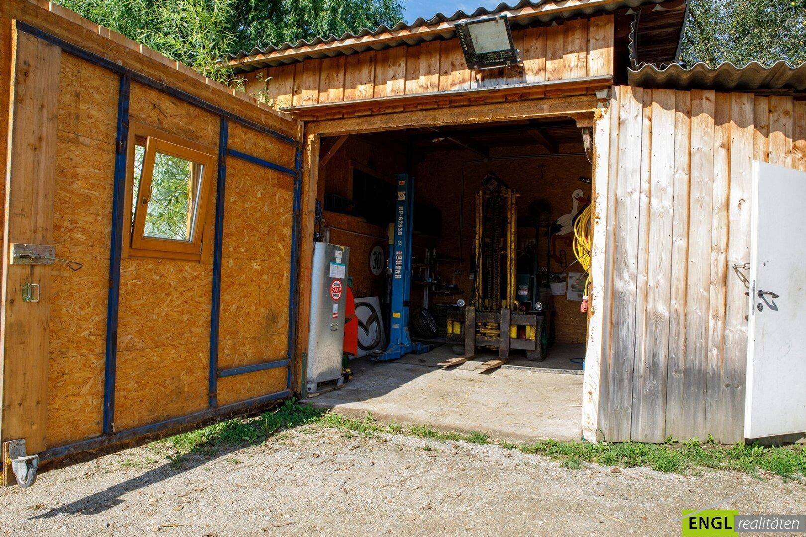 Geräumige Holzgarage oder Werkstatt mit offenem Tor und Hebebühne, ideal für Hobby und Arbeit.