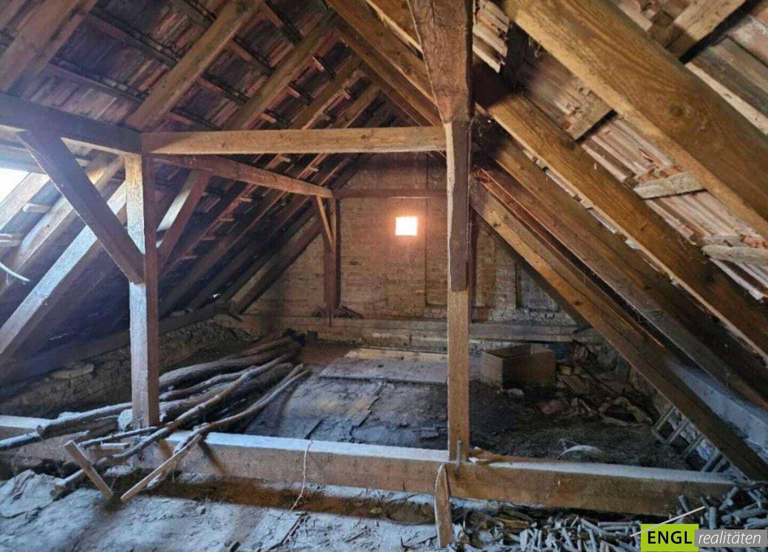 Dachboden mit freiliegender Holzkonstruktion, schrägen Wänden und einem kleinen Fenster.
