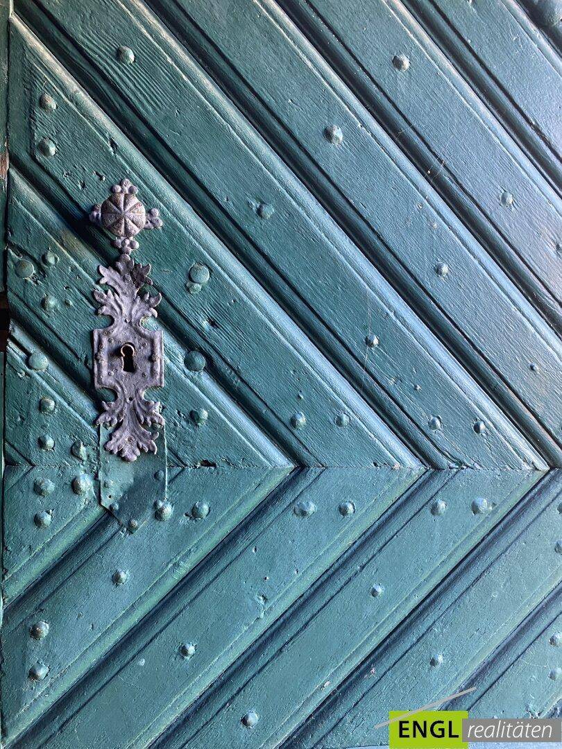 Detailansicht einer alten grünen Holztür mit dekorativem Metallbeschlag und Nieten.