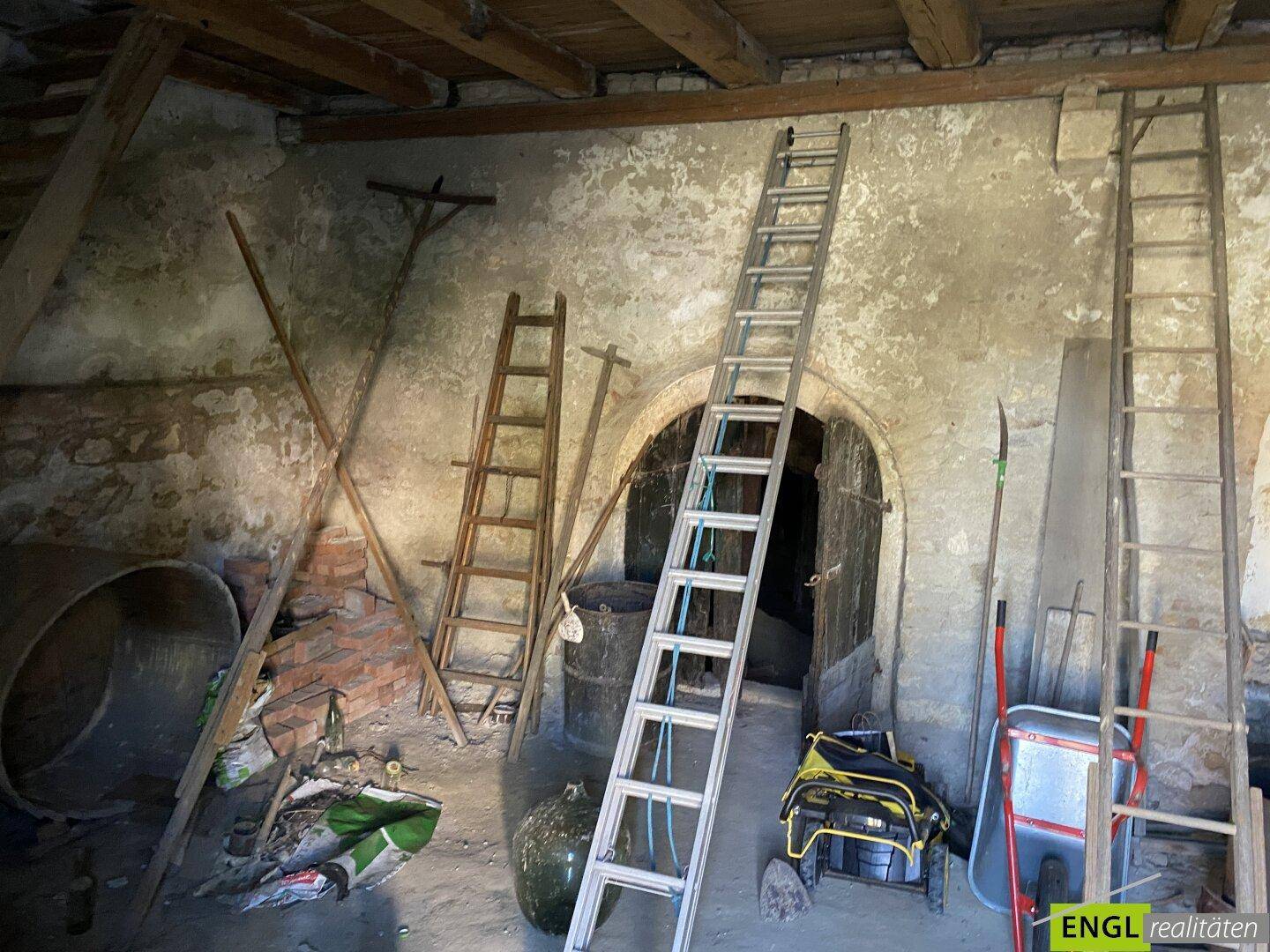 Rustikaler Innenraum mit freiliegenden Holzbalken, unfertigen Wänden und mehreren Leitern.