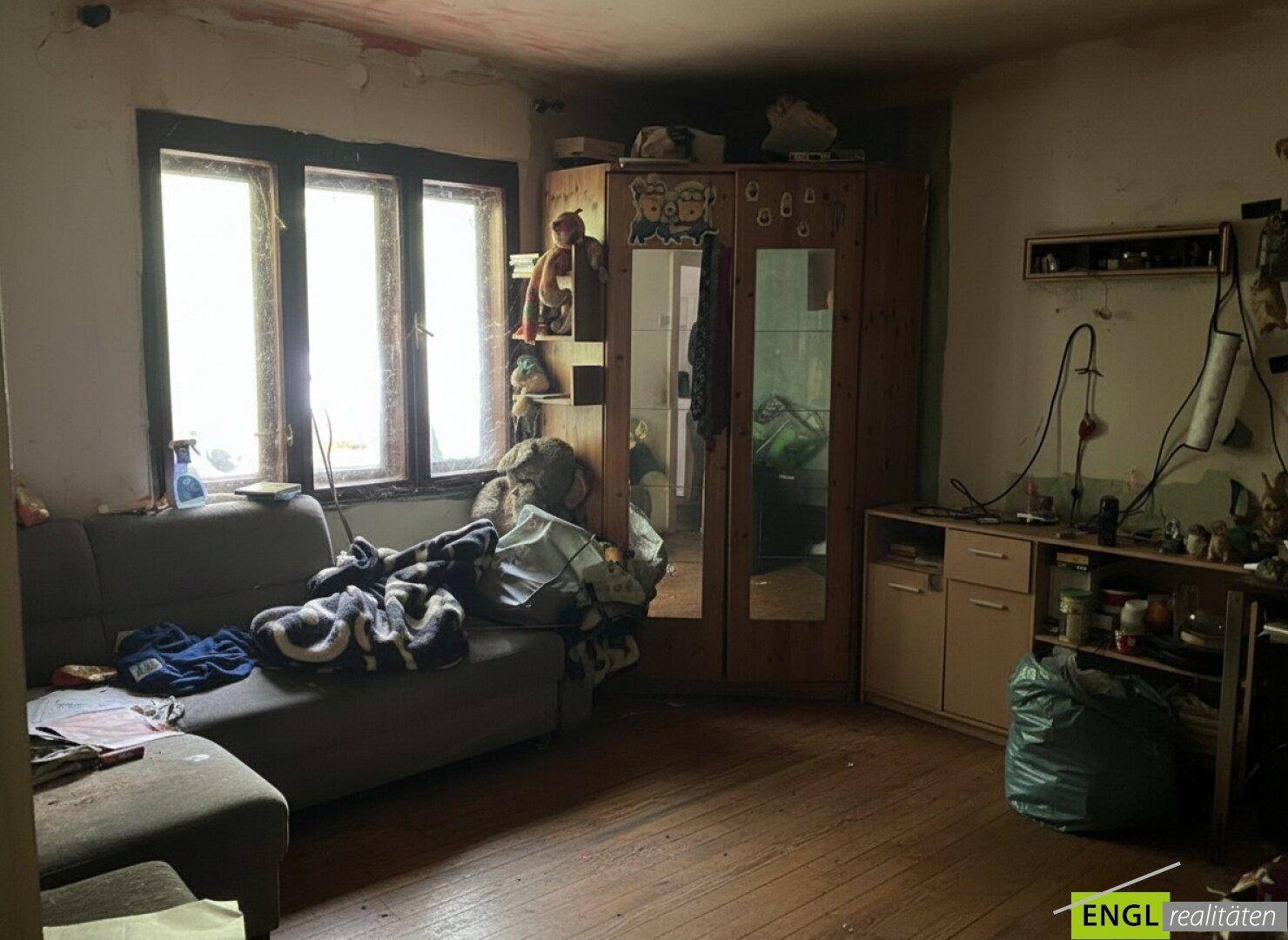 Gemütliches Wohnzimmer mit Sofa, Kleiderschrank und viel natürlichem Licht durch die Fenster.