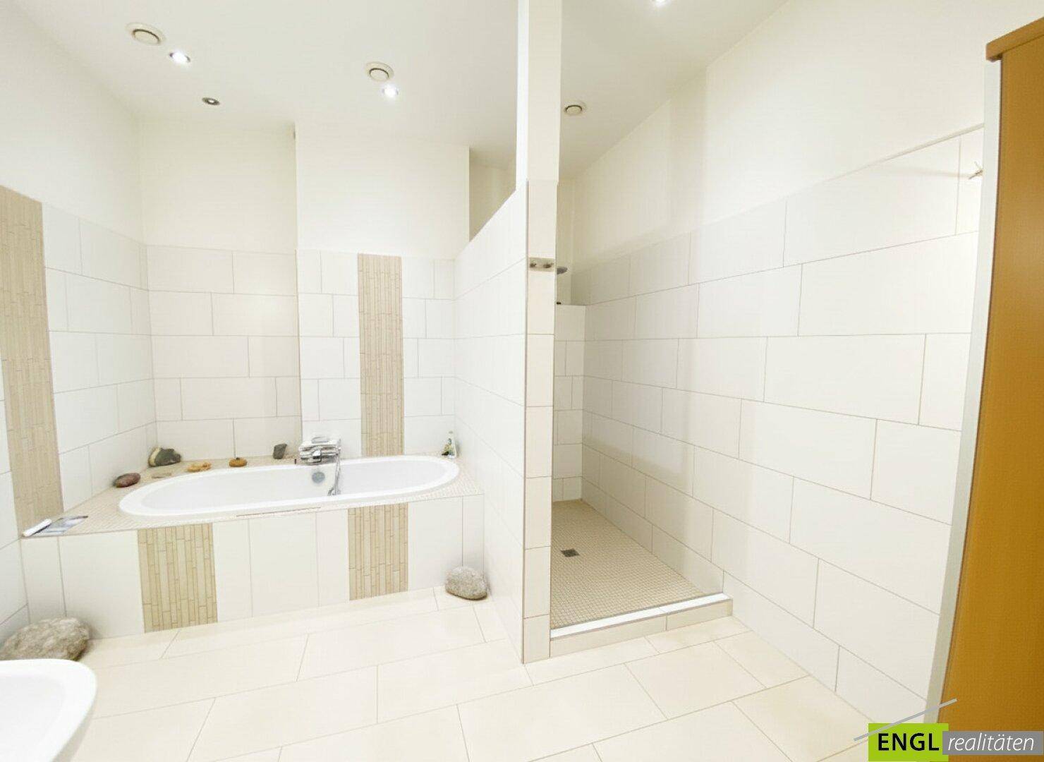 Geräumiges Badezimmer mit Badewanne, begehbarer Dusche und hellen Fliesen an Wänden und Boden.