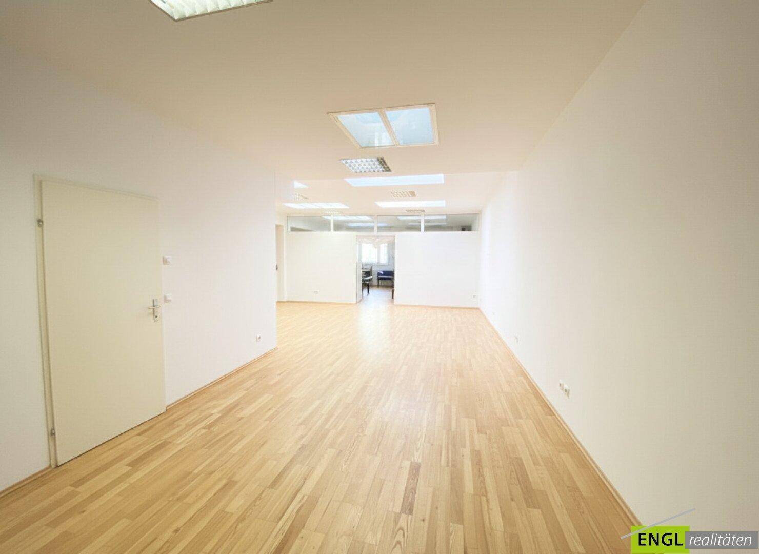 Langer, leerer Büroraum mit Holzboden und weißen Wänden, ideal für flexible Arbeitsplatzgestaltung.