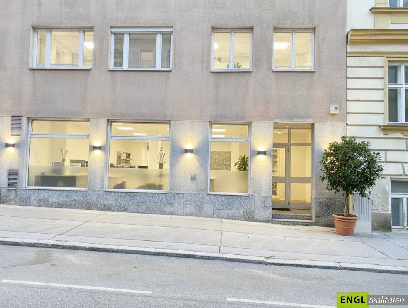 Fassade eines modernen Geschäftsgebäudes mit großen Fenstern und beleuchtetem Eingangsbereich.