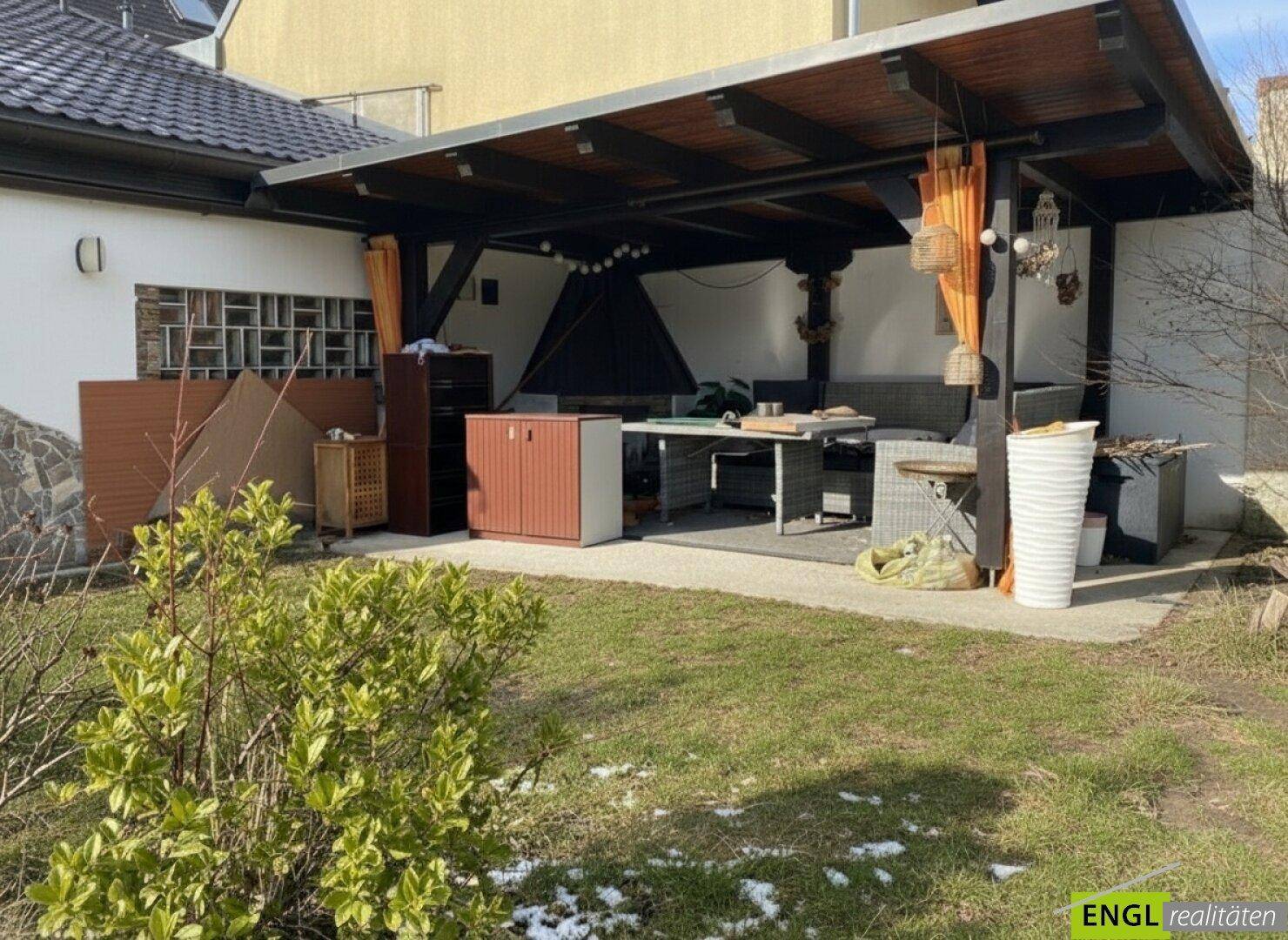 Überdachte Terrasse mit Sitzgelegenheiten und Grillbereich, angrenzend an den Garten.