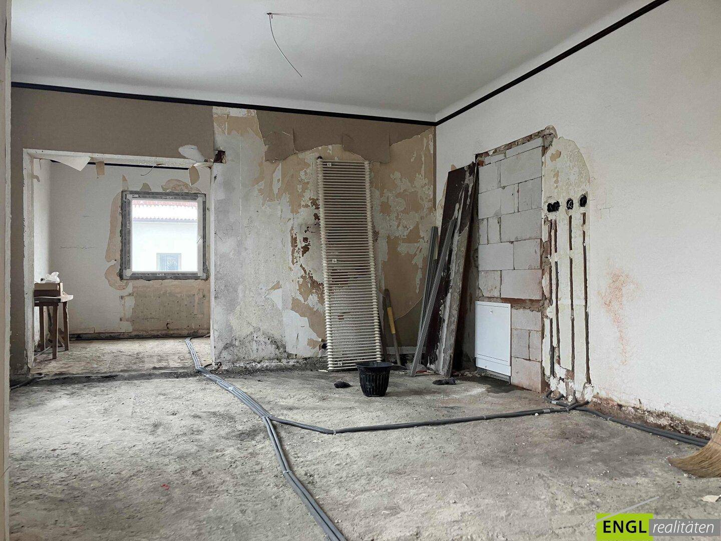 Renovierungsbedürftiger Innenraum mit freigelegten Wänden und Installationsleitungen.