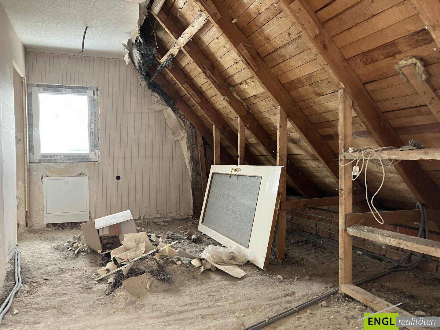 Unausgebautes Dachgeschoss mit sichtbaren Holzbalken und einem Fenster, ideal für den Ausbau.
