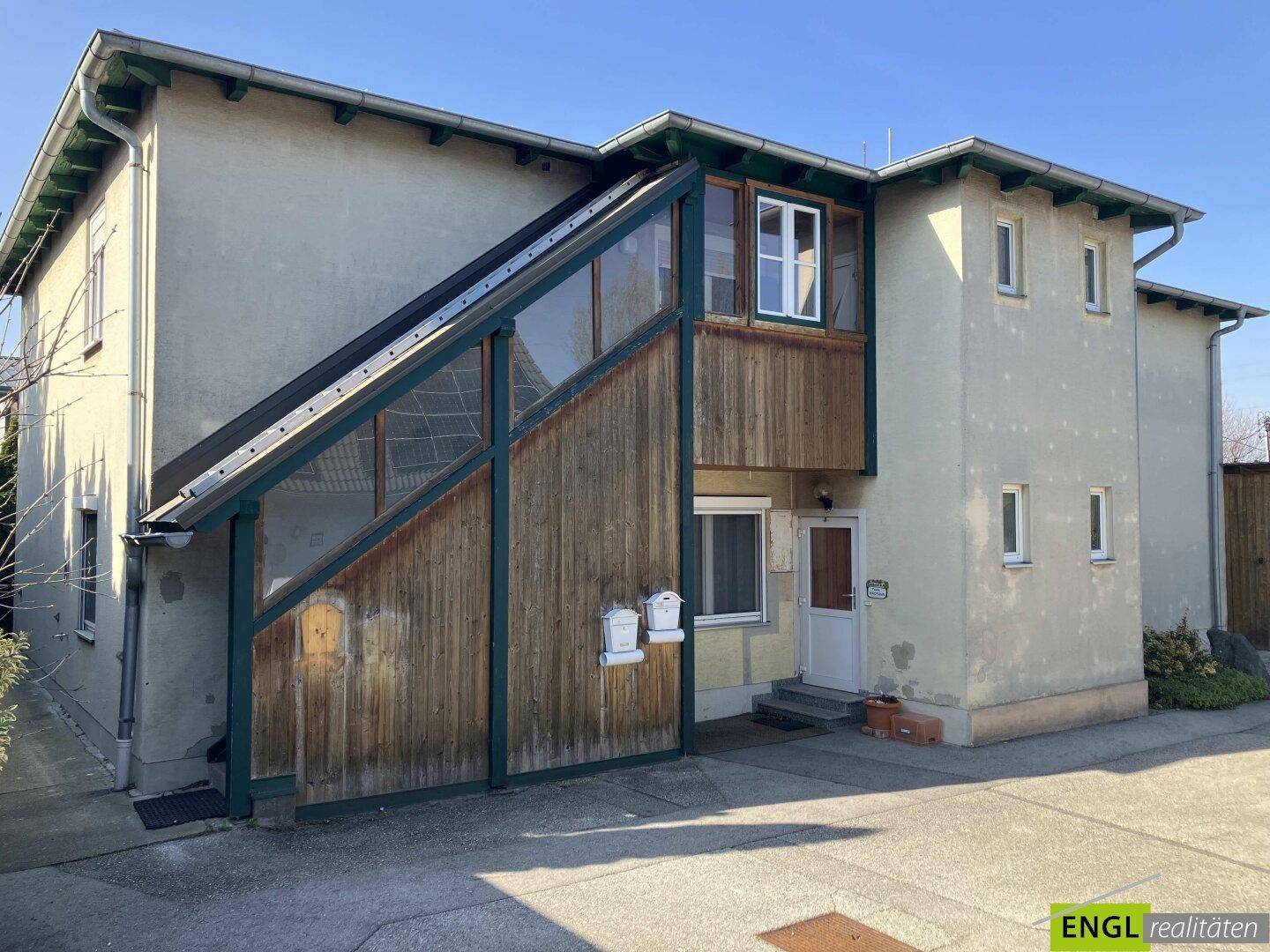 Rückseite des Gebäudes mit Außentreppe und Holzverkleidung, die zu einer oberen Etage führt.
