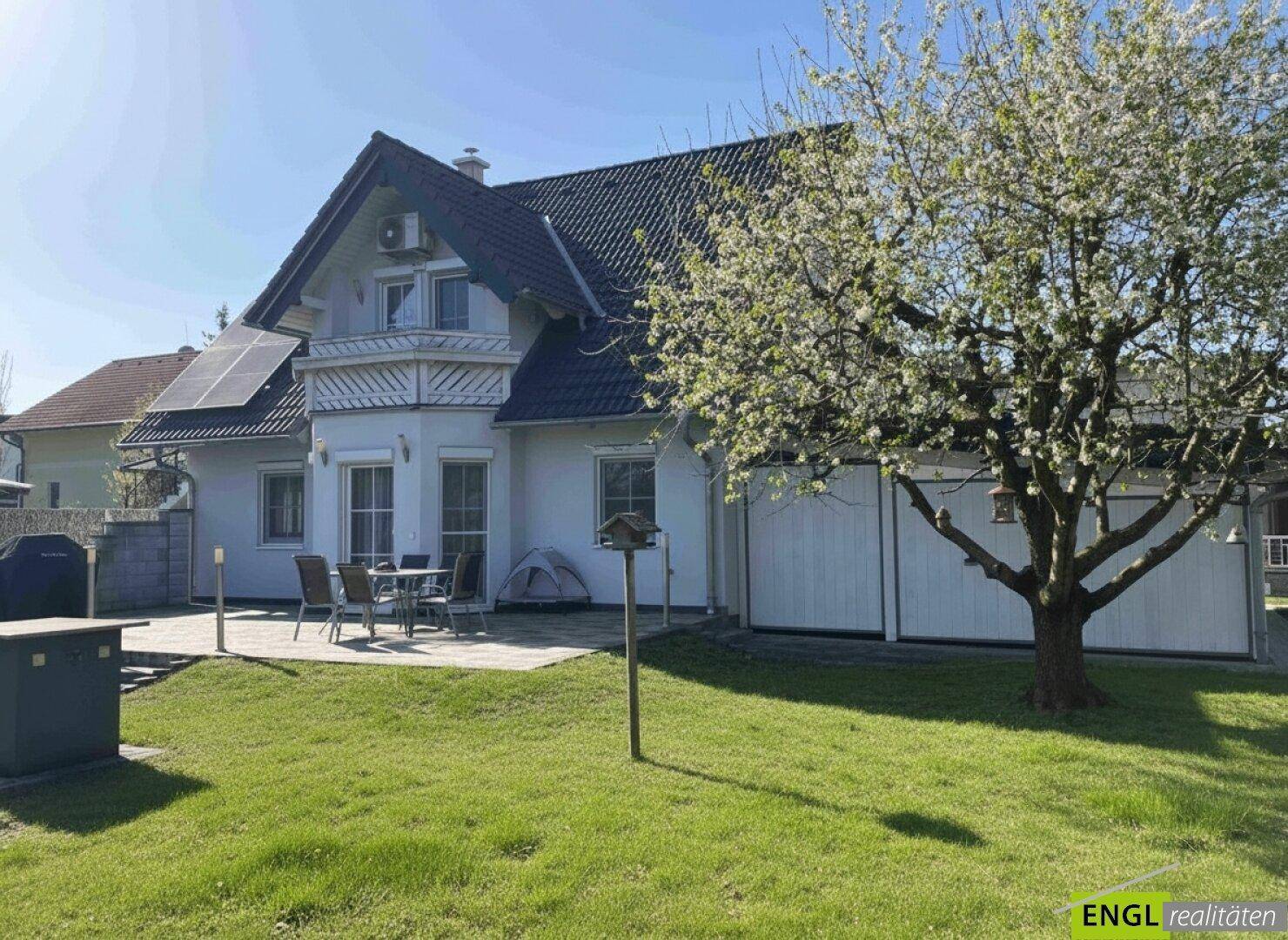 Gepflegter Garten mit Terrasse, blühendem Baum und dem Hauptgebäude im Hintergrund.