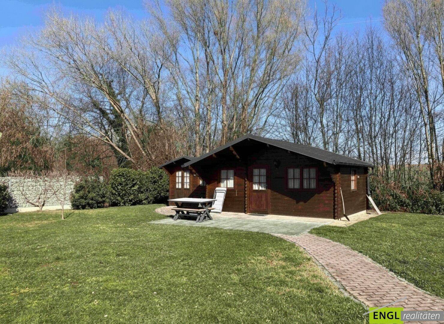 Gemütliches Holzhaus im Garten mit gepflastertem Weg und Sitzgelegenheit im Freien.