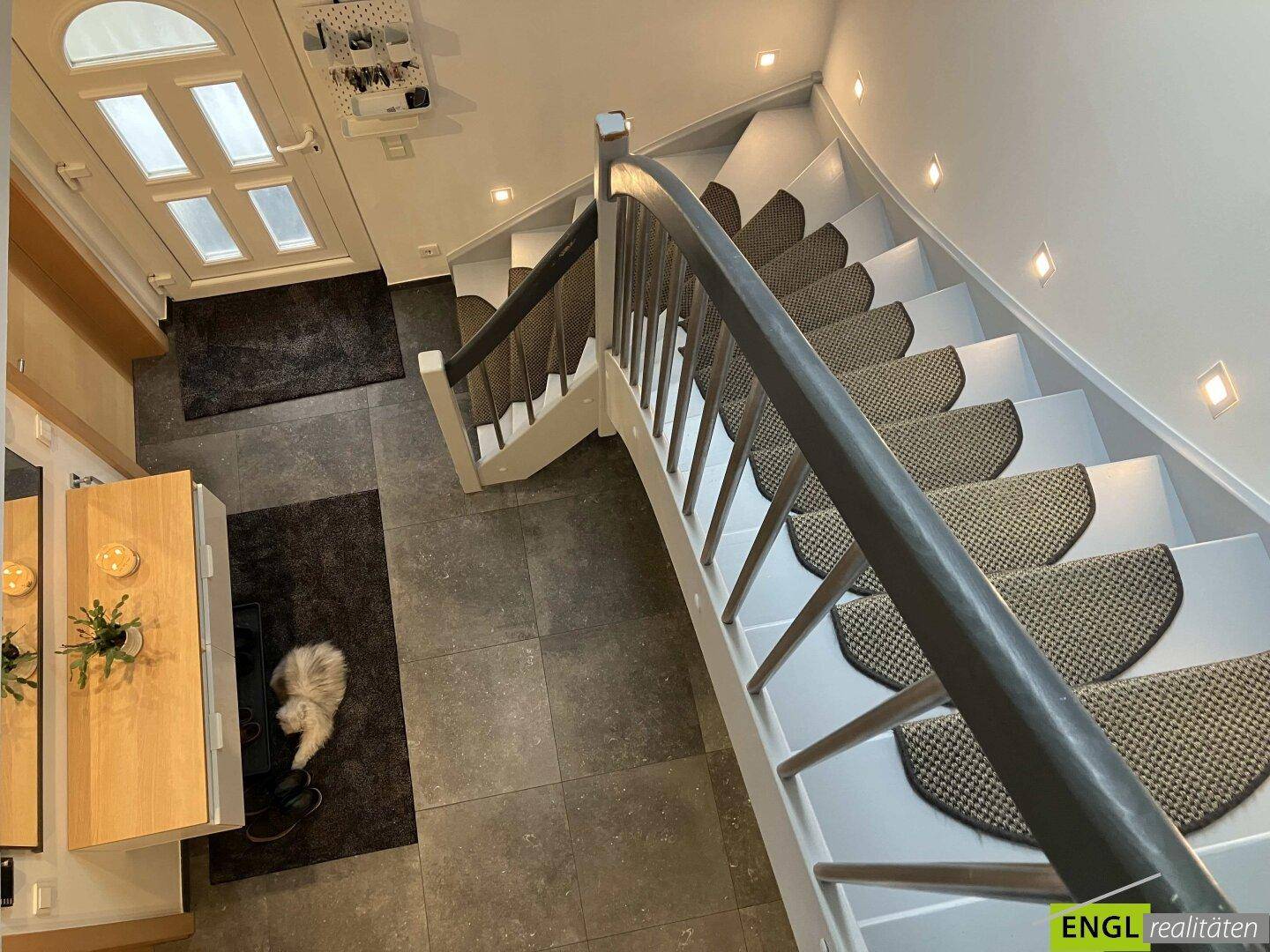 Eingangsbereich mit Treppe, Fliesenboden und Garderobe, hell beleuchtet durch Einbauspots.
