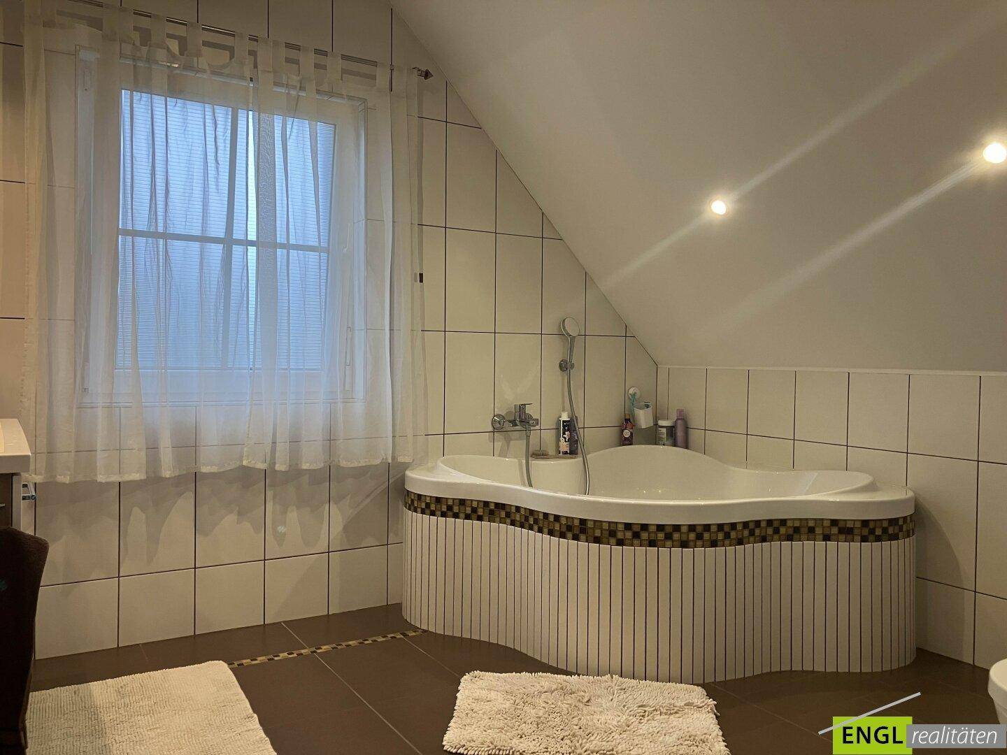 Badezimmer im Dachgeschoss mit Eckbadewanne, Fenster und weißen Fliesen.