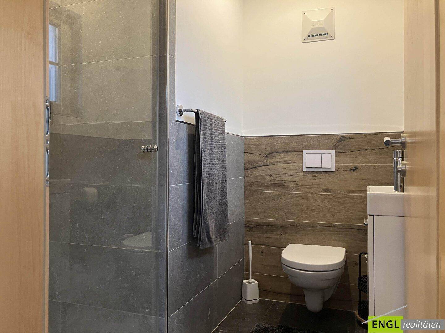 Modernes Badezimmer mit begehbarer Dusche, Wand-WC und stilvollen Fliesen in Grau und Holzoptik.