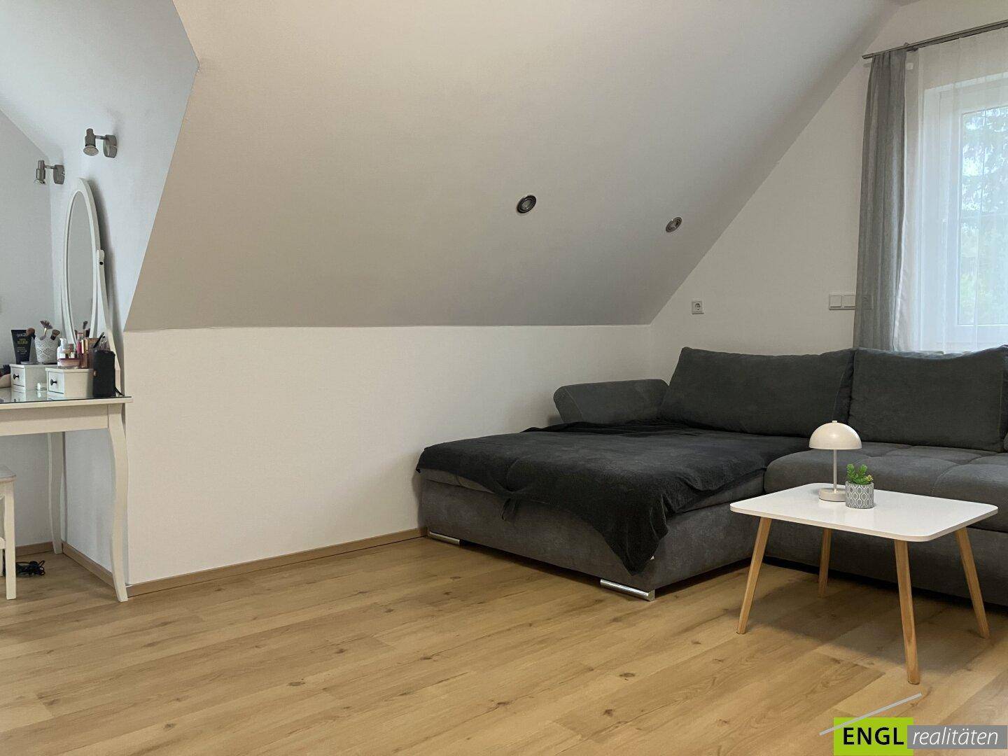 Gemütlicher Wohnbereich im Dachgeschoss mit Schrägdecke, Sofa und kleinem Beistelltisch.