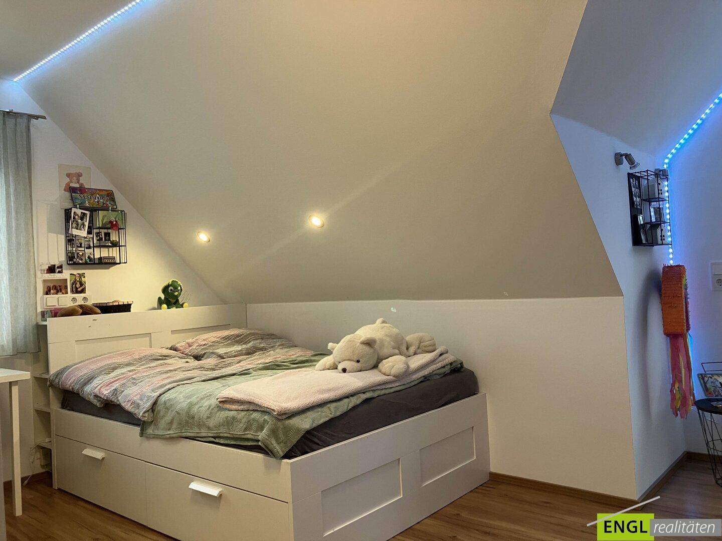 Kinderzimmer im Dachgeschoss mit Bett, Stauraum und dekorativer LED-Beleuchtung.