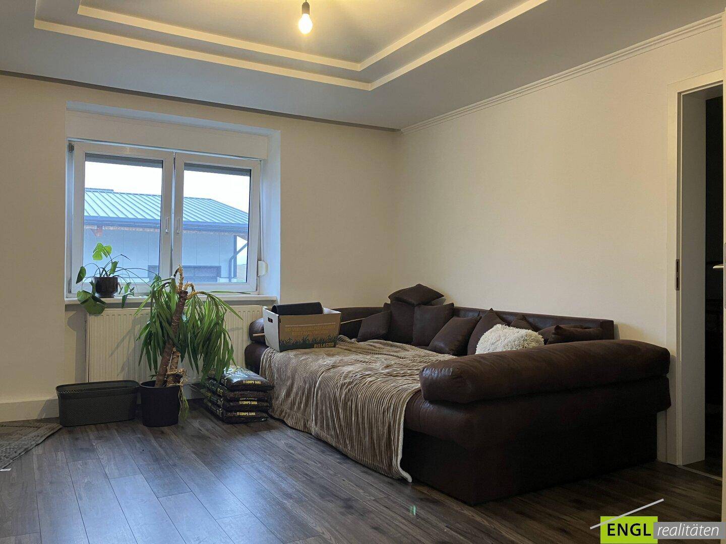 Geräumiges Wohnzimmer mit großem Sofa, Holzboden und Fenster mit Blick nach draußen.