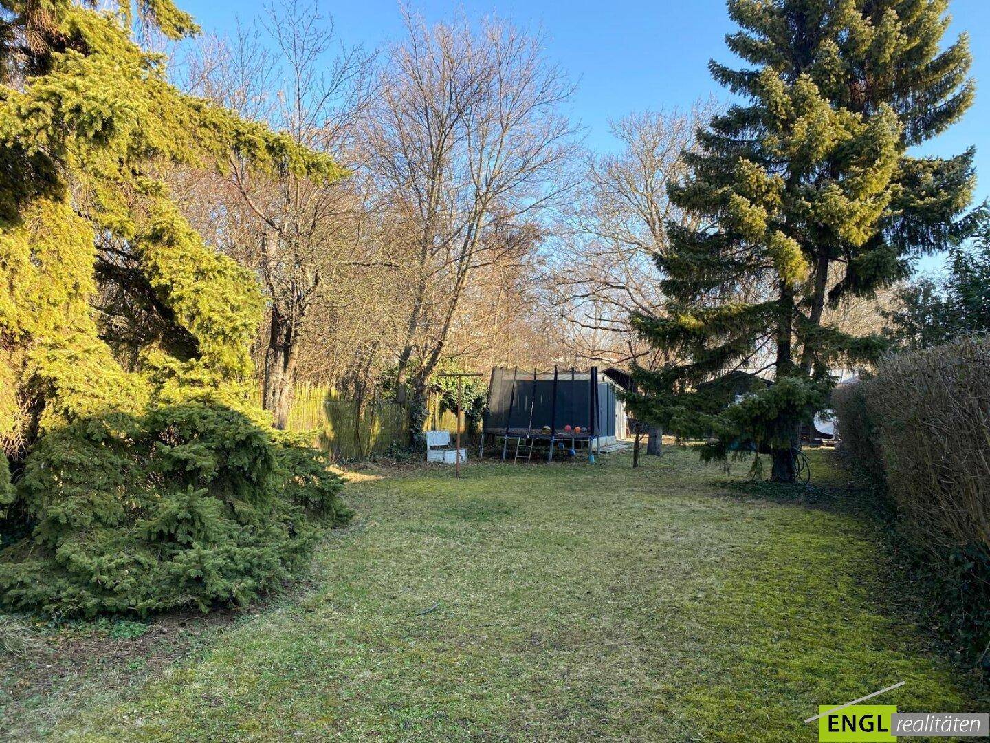 Geräumiger Garten mit Rasenfläche, hohen Bäumen und einem Trampolin für Freizeitaktivitäten.