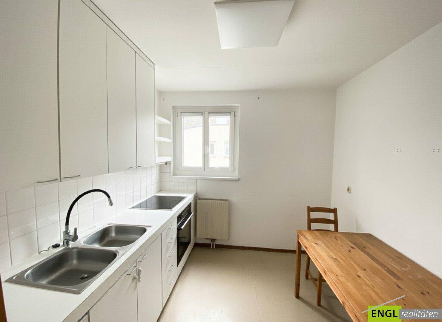 Funktionale Küche mit weißen Schränken, Doppelspüle und einem Essbereich am Fenster.