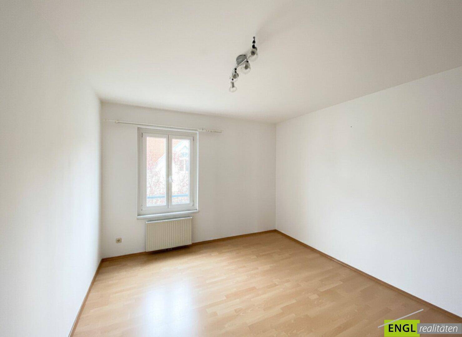 Leeres Zimmer mit Parkettboden und einem großen Fenster, ideal als Schlaf- oder Arbeitszimmer.