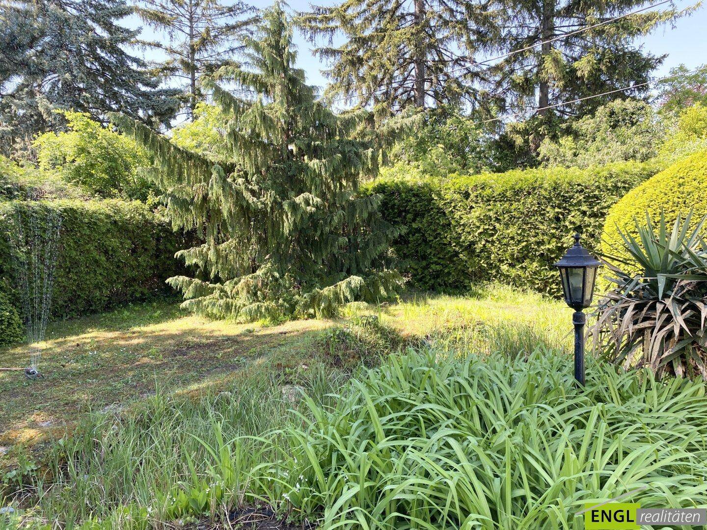 Naturbelassener Gartenbereich mit hohen Gräsern, Bäumen und einer klassischen Gartenlaterne.