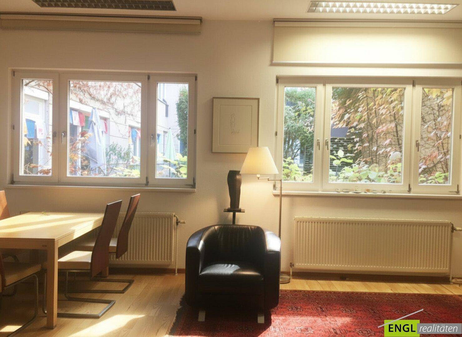 Büroraum mit Esstisch, Sessel und Blick ins Grüne durch große Fenster.