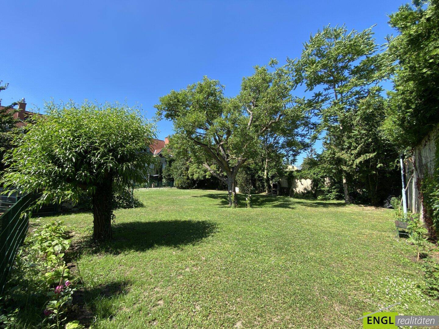 Großer, sonniger Garten mit weitläufiger Rasenfläche und altem Baumbestand, ideal zum Entspannen.