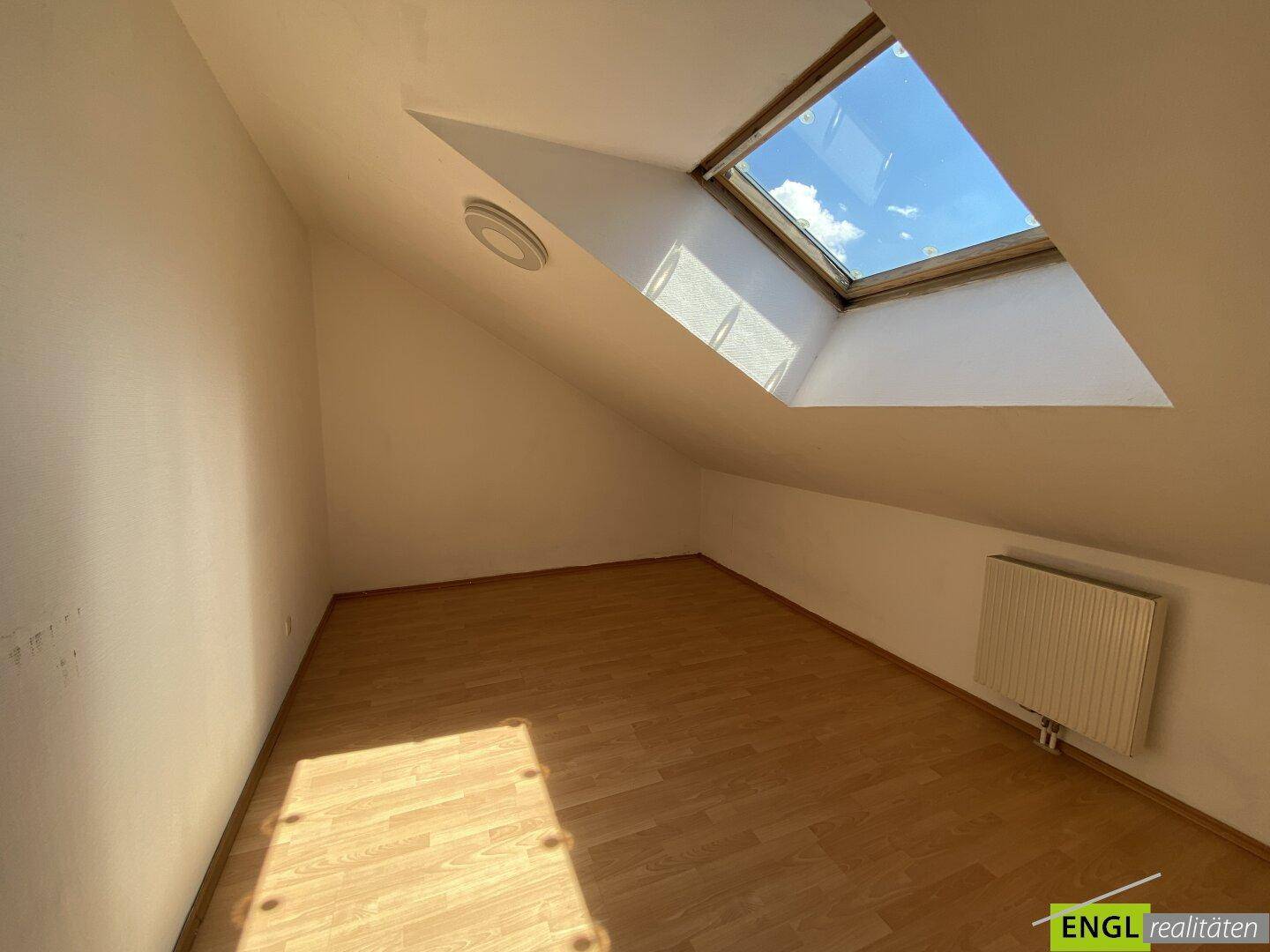 Helles Dachzimmer mit schräger Decke, Dachfenster und Laminatboden, bereit zur individuellen Gestaltung.