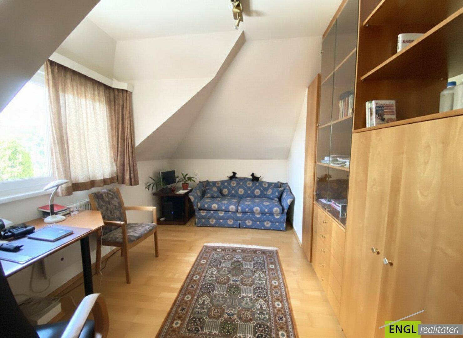 Arbeitszimmer im Dachgeschoss mit Schreibtisch, Sofa und integrierten Regalen, hell und funktional.
