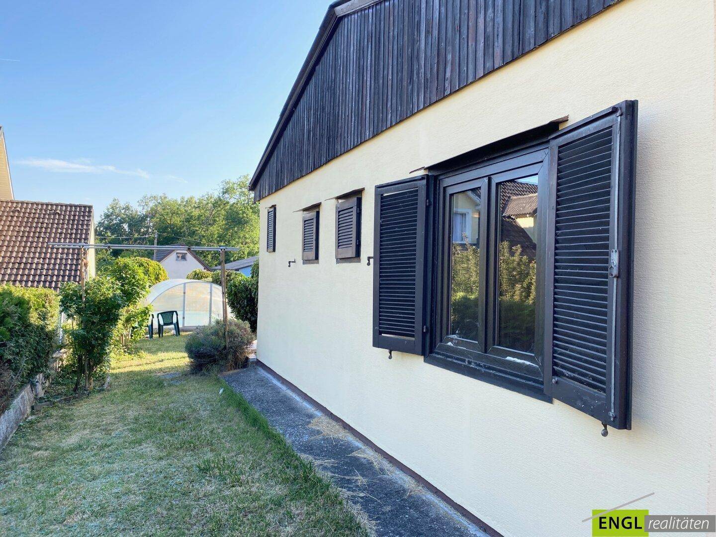 Seitenansicht des Hauses mit geschlossenen Fensterläden und Blick auf den Garten mit Pool.
