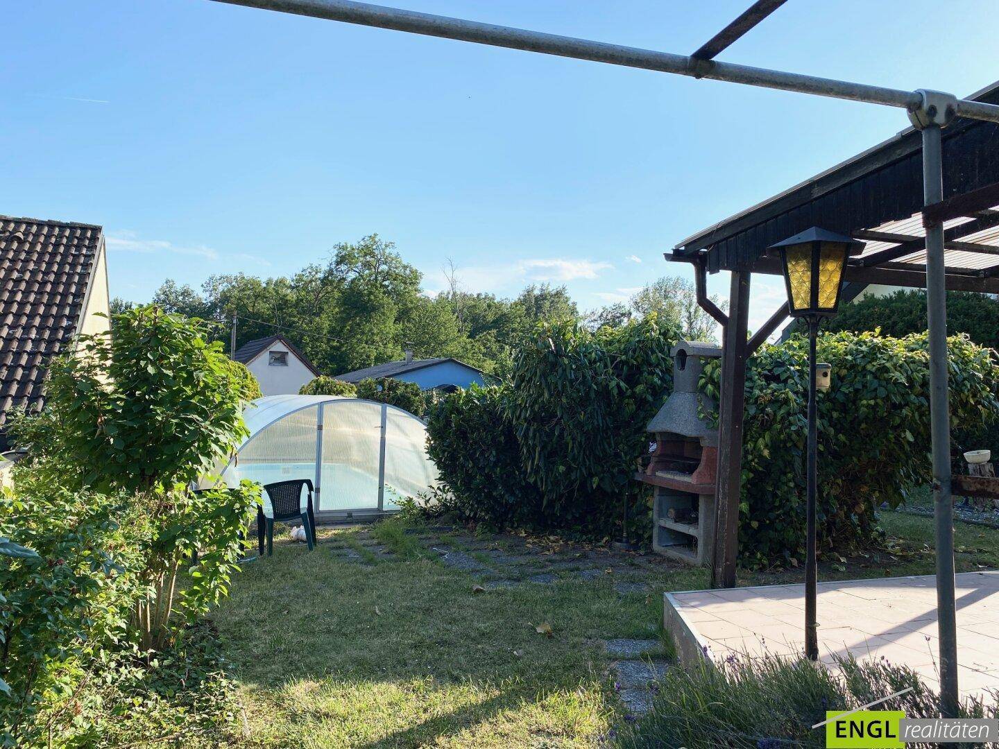 Weitläufiger Garten mit Poolabdeckung, Grillplatz und Zugang zur überdachten Terrasse.