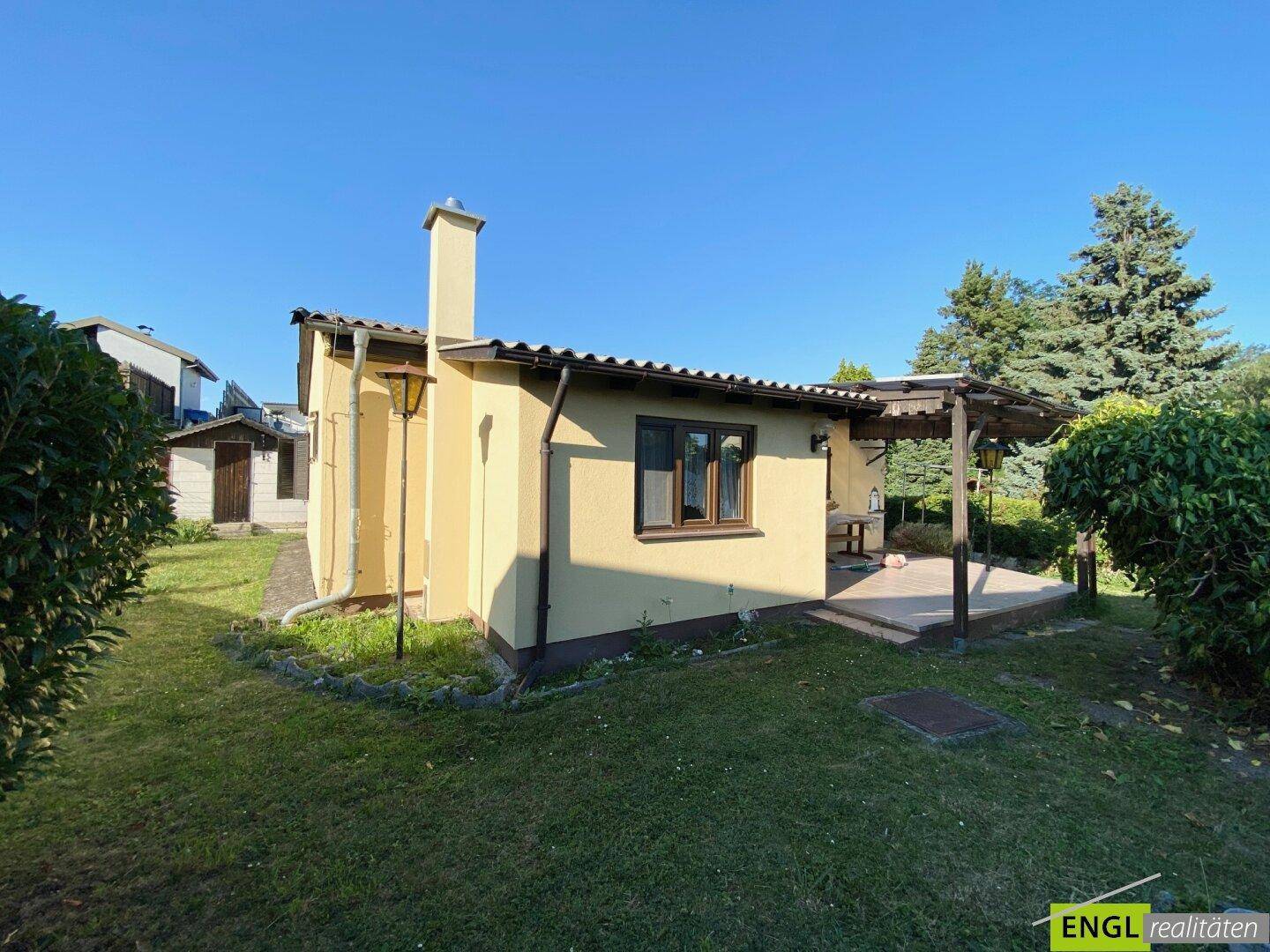 Rückansicht des Hauses mit überdachter Terrasse, Kamin und weitläufigem Garten.