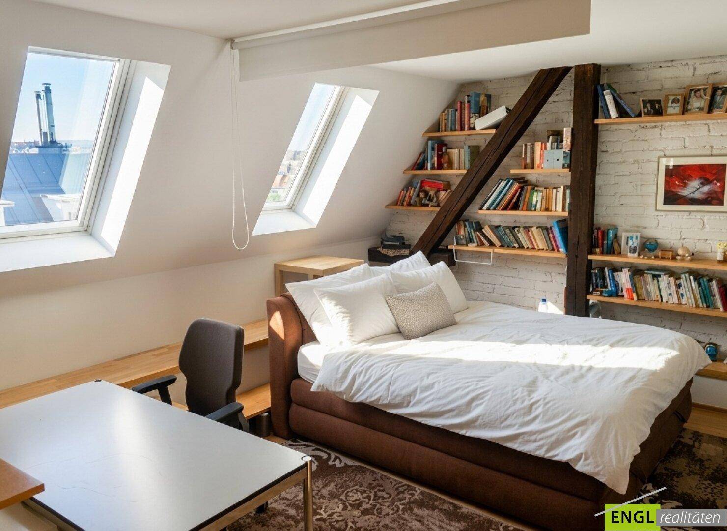 Gemütliches Schlafzimmer mit Dachschrägen, Einbauregalen und zwei Dachfenstern.