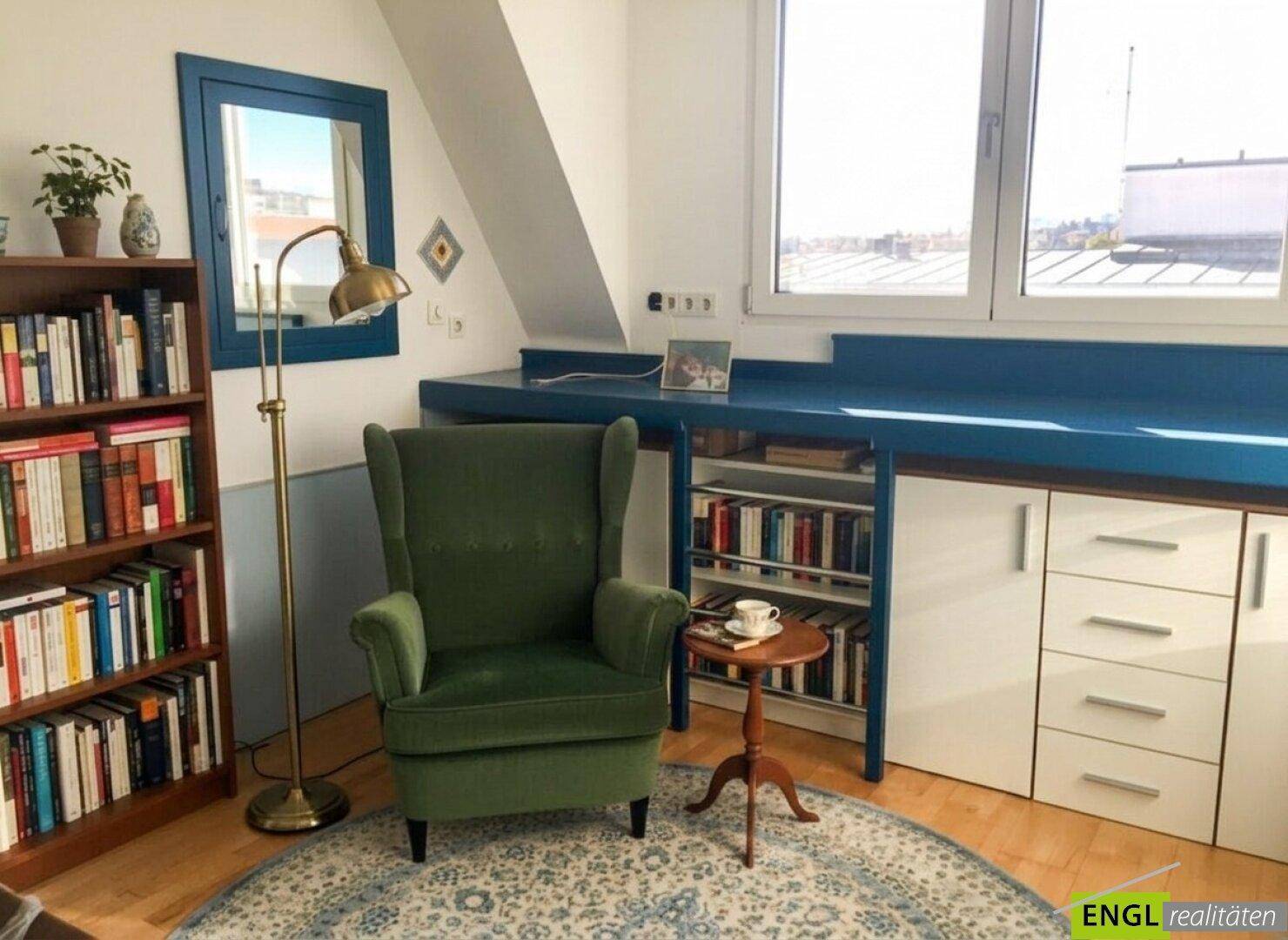 Leseecke mit grünem Sessel, Bücherregalen und großem Fenster mit Ausblick.