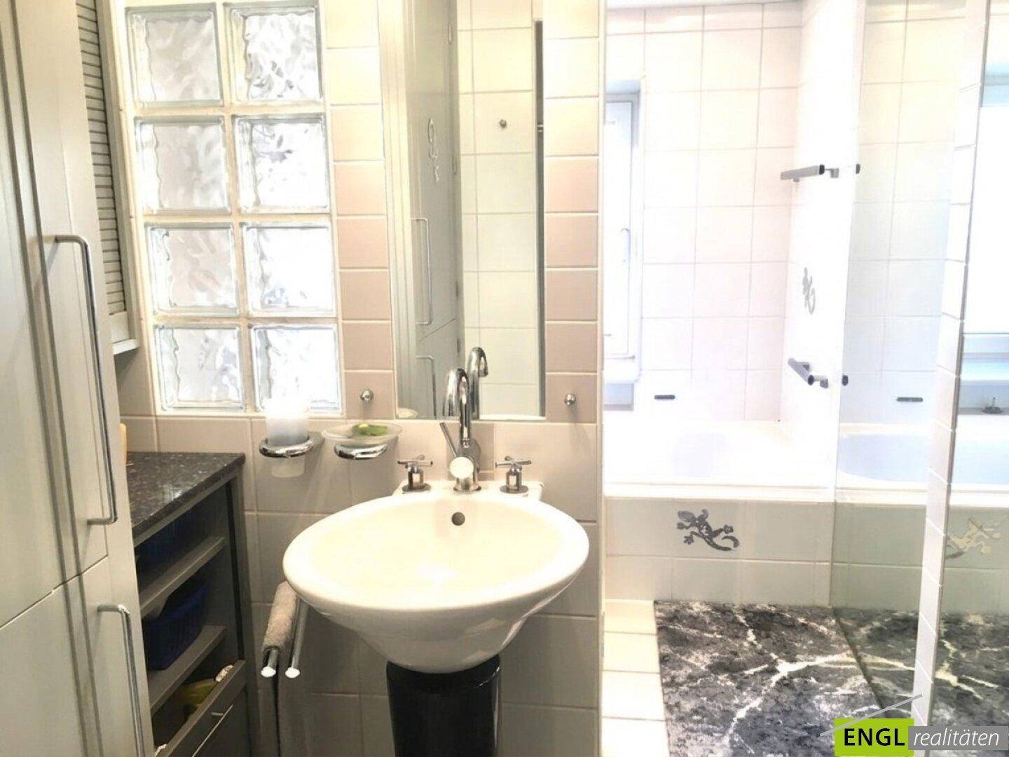 Helles Badezimmer mit Waschbecken, Badewanne und Glasbaustein-Fenster.