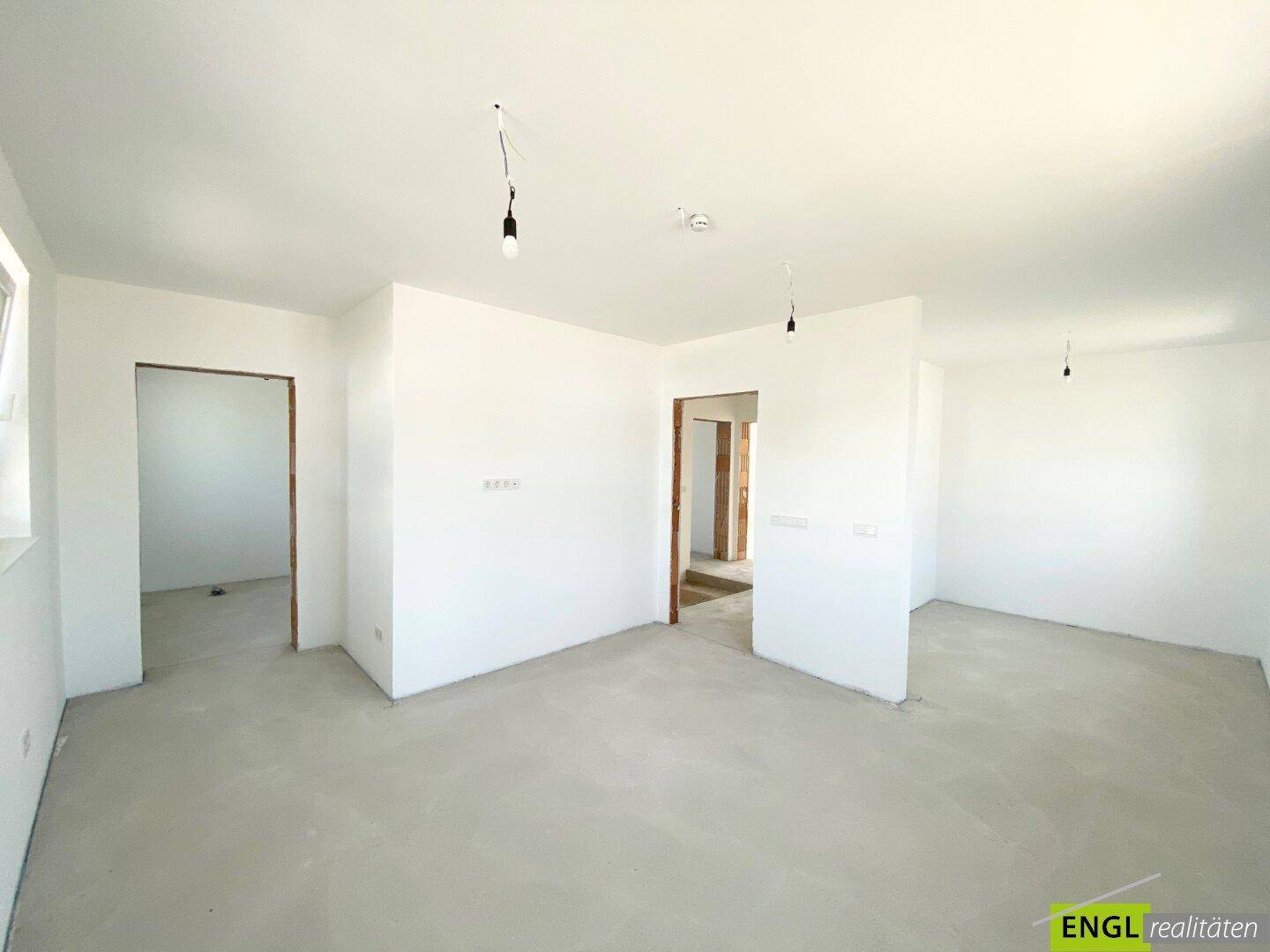 Offener Wohnbereich mit mehreren Zugängen zu anderen Zimmern und viel Tageslicht im Neubau.