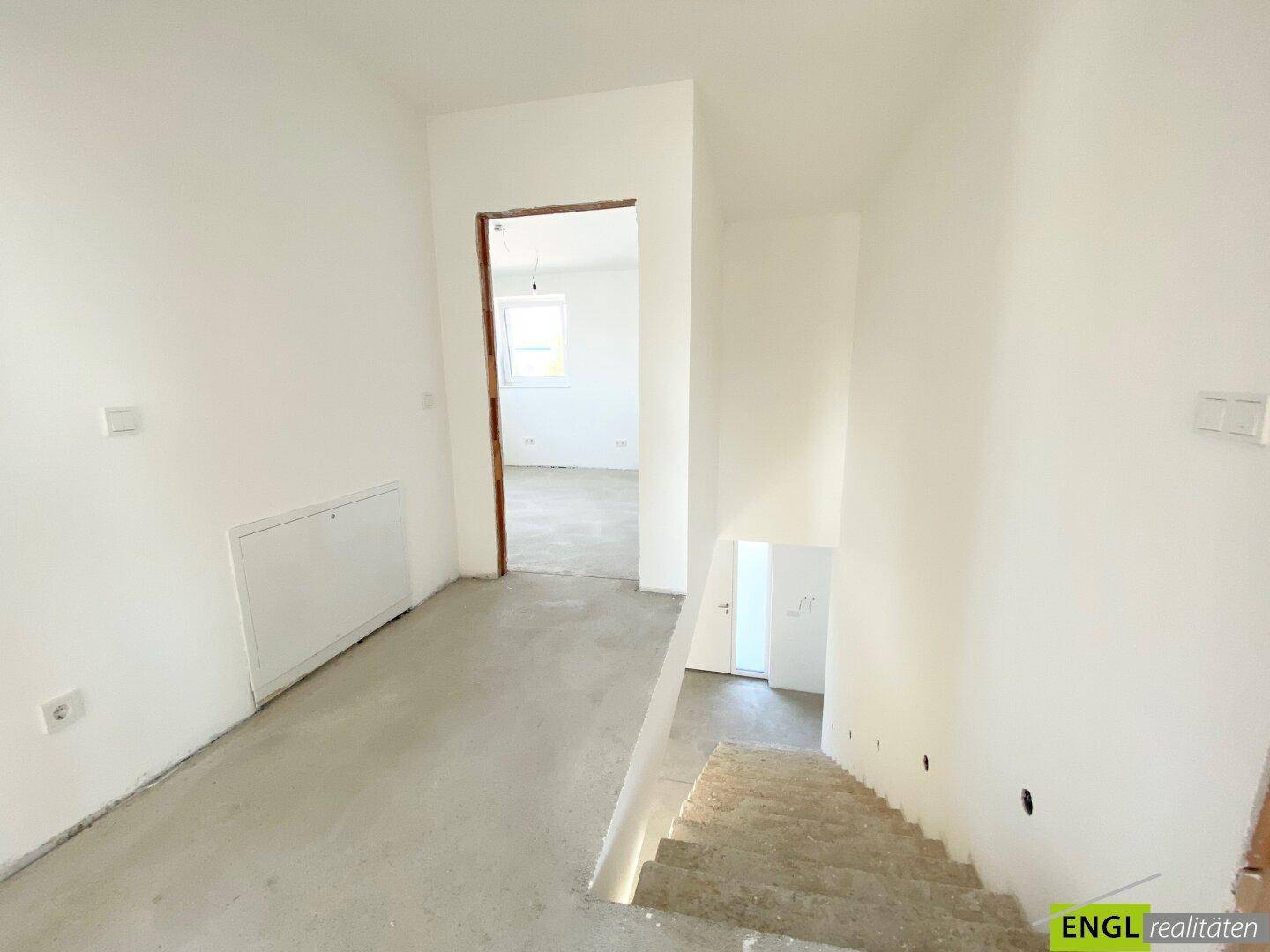 Heller Flur mit Treppenabgang und Zugang zu weiteren Räumen im Neubau, noch im Rohbauzustand.