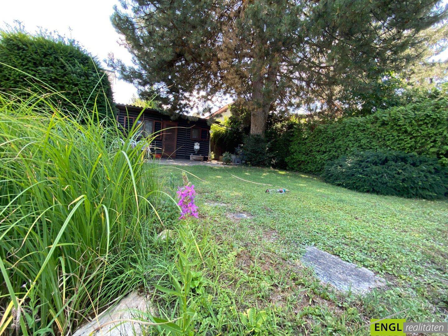 Blühender Gartenbereich mit üppiger Vegetation, Rasenfläche und Blick auf das charmante Gartenhaus.