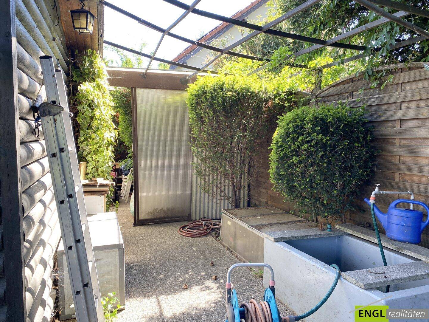 Überdachter Außenbereich mit Waschbecken, Stauraum und praktischen Gartenutensilien.